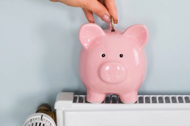 Evdeki radyatörün üstündeki kumbaraya para sokan bir kadının yakın çekimi.