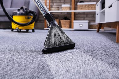 Evdeki elektrikli süpürgeyi kullanarak oturma odasındaki insan temizleme halısı.