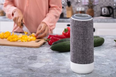 Mutfakta sebze doğrayan kadının önünde kablosuz hoparlör.