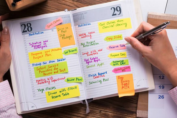 Close-up Of Businesswoman Writing Schedule In Calendar Diary On Desk