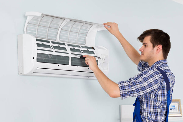 Woman Looking At Young Male Technician Servicing Or Repairing Air Conditioner At Home