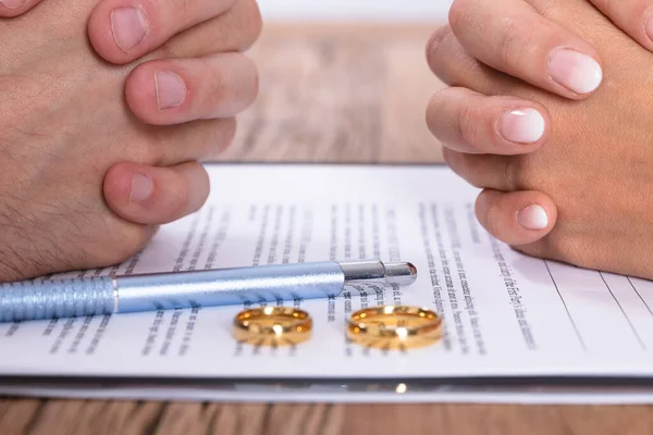 Couple's Hand With Divorce Agreement And Golden Wedding Rings On Wooden Desk