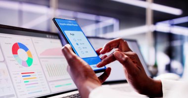 Çevrimiçi burs için başvuran Afrikalı Öğrenci, Form Doldurma Kolej Finans Ofisi 'nde siyah telefon ve dizüstü bilgisayarla.