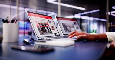 Amerikalı Kadın Siyah ve Beyaz Odadaki Kanepede dinlenirken Dizüstü bilgisayardaki ve telefondaki Haberlere Bakıyor