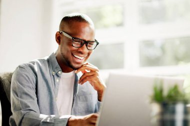 Ofis masasında dizüstü bilgisayarda çalışan Afrikalı Amerikalı iş adamı, şirketi için pazarlama stratejileri planlıyor, liderlik ve yenilik gösteriyor.