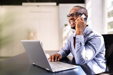 Gülümseyen Afro-Amerikalı iş adamı masadaki akıllı telefonda çoklu görev yapıyor, İK sözleşmesi için müşteriyle internet üzerinden iletişim kuruyor..