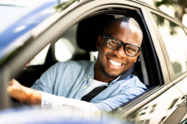 Gülümseyen Afrikalı Amerikalı adam, gururla yeni arabasını sürerken, bir CEO olarak yeteneklerini sergiliyor..