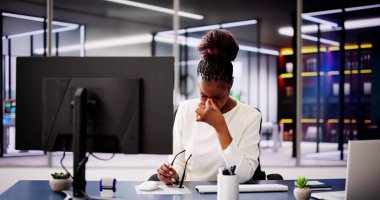 Ofiste bilgisayar üzerinde çalışırken göz ağrısıyla boğuşan Afrika kökenli Amerikalı kadın semptomlara karşı rahatlama arıyor..