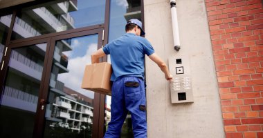 Bina girişinde güvenli teslimatlar için gelişmiş dahili iletişim sistemi kullanan profesyonel kurye, kimlik doğrulama ile paketlerin teslim edildiğinden emin olur.