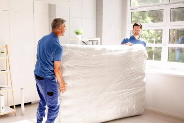 Yetenekli nakliyeciler emlak kiralama şirketinin yatak odasına yeni bir yatak götürerek takım çalışması ve iç dekorasyon sergiliyorlar..