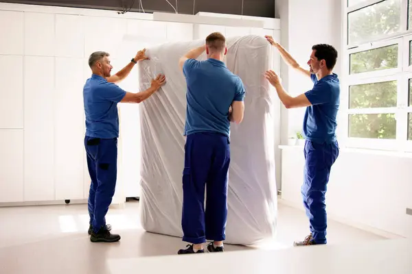 stock image A team of professional movers in uniforms delivering furniture to a happy customer's new bedroom. professions: mover, delivery, designer, packer