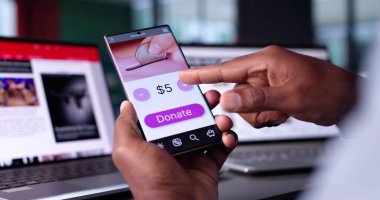 Afrikalı Amerikalı adam internet üzerinden para bağışlamak, hayır kurumlarını desteklemek ve finans fonlarına yatırım yapmak için akıllı telefon uygulaması kullanıyor..