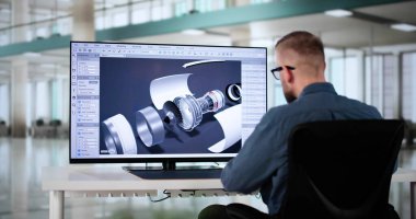 Erkek Mühendis, fabrika ofisinde dizüstü bilgisayarda 3D CAD yazılımı kullanarak mekanik parçalar geliştiriyor.