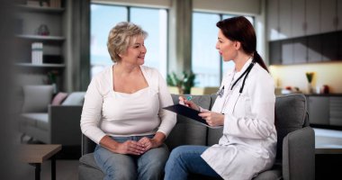 Doktor evde yaşlı bir hastayla konuşuyor.