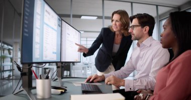 Afrikalı Amerikalı kadın elektronik faturaları yönetmek için bilgisayar yazılımı kullanıyor. Ofis müdürü ve muhasebeci mali durum analizinde işbirliği yapıyor.