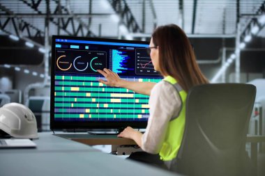 Modern otomatikleştirilmiş fabrikada gelişmiş robot kolu kullanan genç bir kadın..