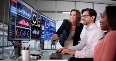 Çeşitli öğretmenlerle bilgisayar ekranlarındaki verileri analiz eden işletme öğrencileri.