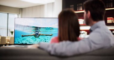 Çift koltukta dinleniyor, evde televizyon seyrediyor..