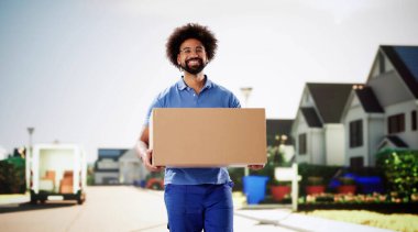 Gülümseyen kurye posta kamyonuyla bir paket teslim ediyor. Üniformalı genç adam teslimat için bir kutu tutuyor.