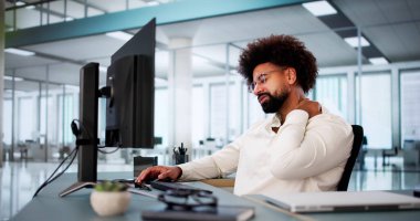 Ofis bilgisayarının arkasında boynu ağrıyan profesyonel Afro-Amerikan işadamı.