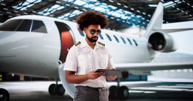 Uçuş öncesi kontrol listesi için tablet kullanan neşeli Afro-Amerikan pilot.