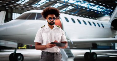 Uçuş öncesi bakım için tablet kullanırken gülümseyen profesyonel Afro-Amerikan pilot.