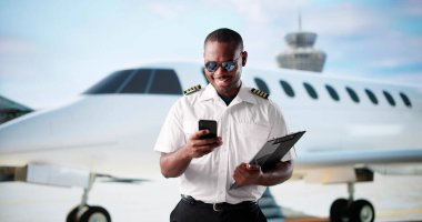 Afrikalı Amerikalı Pilot, özel jete binmeden önce havaalanında gülümsüyor.