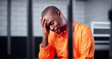 Parmaklıklar ardında hapsolmuş, Afro-Amerikalı bir adam hapiste ağlıyor. Suç ve Ceza Pişmanlık Hücresinde Çarpıştı