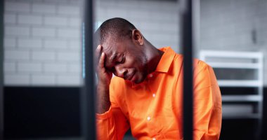 Turuncu üniformalı Afro-Amerikan Mahkûm Parmaklıklar Arkasında Ağlıyor.