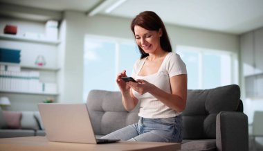 Genç kadın koltukta oturuyor, cep telefonunu tutarken gülümsüyor.