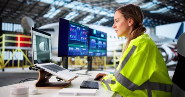 Kadın Mühendis Havacılık Hangarında Dizüstü bilgisayarın motor planlarını analiz ediyor.