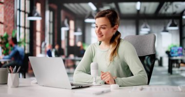 Ofis bilgisayarında mutlu çalışan beyaz kadın portresi. Bir Webinar 'a katılıyor, not alıyor.