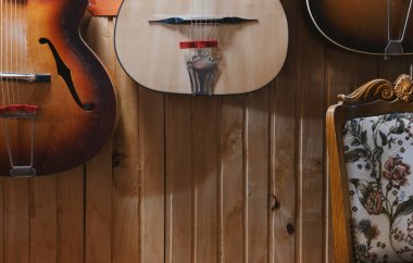 Parts of three old acoustic guitars and decorated chair in front of a wooden wall. clipart