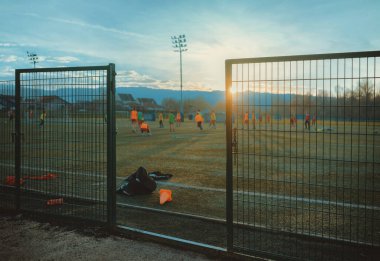 Genç oyuncular antrenman yaparken futbol sahasının girişinin önünde..