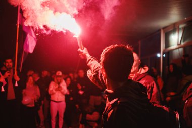 Elinde meşale tutan genç bir adam, arka planda bir grup insan, bir gece sahnesi..