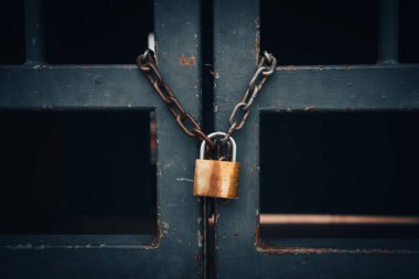 Eski bir çitin paslı parmaklıkları arasındaki zincirin üzerinde bronz bir metal kilit..