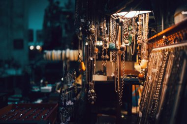 Mağazadaki bir rafta el yapımı mücevherler, bir lamba ve arka plandaki odanın içi ile aydınlatılmış..