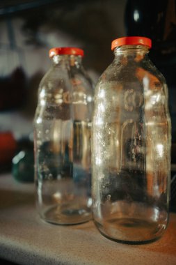Mutfak masasında kırmızı başlıklı iki boş cam şişe..