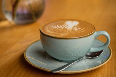 Kapuçino ve pastel mavi seramik bardaktaki latte sanatı kırsal ahşap masada. Samimi, minimalist kahve sahnesi, sabah ayinleri ve kahve dükkanı yaşam tarzı için ideal..