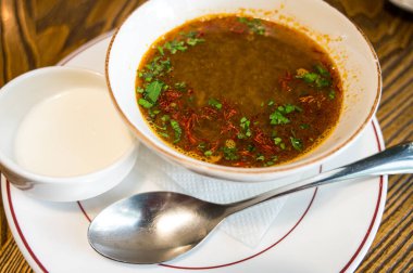 Bitkilerle ve safranla kaplanmış zengin geleneksel çorba, yanında ekşi kremayla servis edilen sıcak bir restoran ortamında..