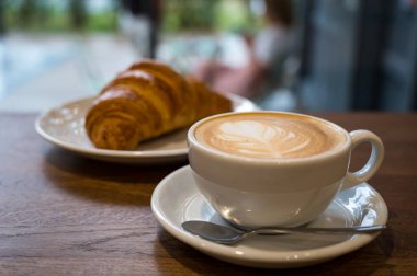 Sütlü kahve sahnesi ve ahşap masa üzerinde gevrek kruvasan, kahvaltı veya kahve molası için mükemmel..