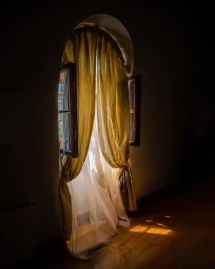 Altın perdeleri olan zarif kemerli pencere ve güneş ışığı, iç dekorasyon ve yaşam tarzı arka planıyla aydınlatılan katıksız kumaş..