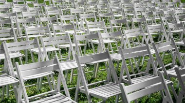 Yeşil çimenlere dizilmiş beyaz katlanır sandalyeler, etkinlik, seremoni veya performans için açık hava düzenlemesi, soyut yineleme arka planı.