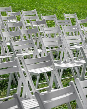 Yeşil bir çimenlikte sıra sıra dizilmiş çok sayıda beyaz katlanır sandalye, açık hava koltukları etkinlik, düğün, festival veya tören için hazırlanır.