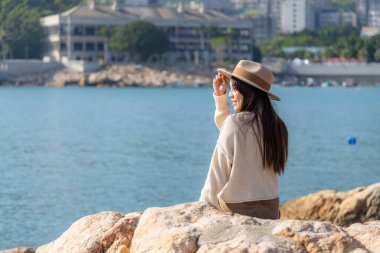 Kadın kayaya otur ve deniz manzarasının tadını çıkar.