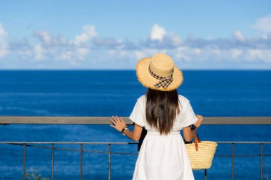 Beyaz elbiseli kadın ve mavi gökyüzü ile deniz manzarasının tadını çıkar.