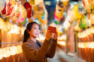 Kadın cep telefonuyla bir sürü fenerle fotoğraf çekiyor.