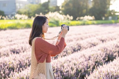 Kadın çiçek tarlasında fotoğraf çekmek için kamera kullanıyor.