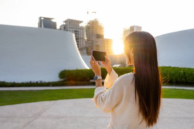 Kadın gün batımında gün ışığıyla fotoğraf çekmek için cep telefonu kullanıyor.