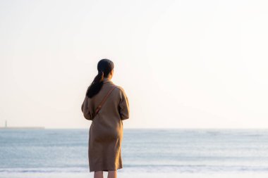 Kadın sahilde durup gün batımını izliyor.